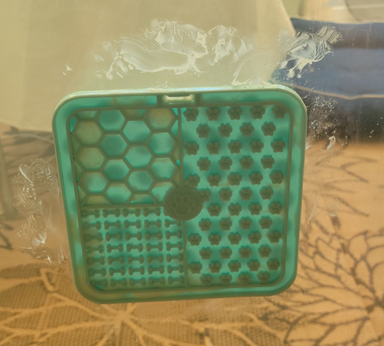 The mint-green lick mat stuck to a glass door, surrounded by dried yoghurt splatter marks on the glass
